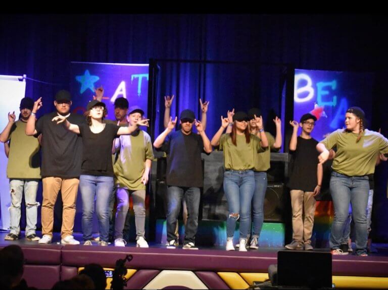 Students performing in matching t-shirts on a stage with blue lighting